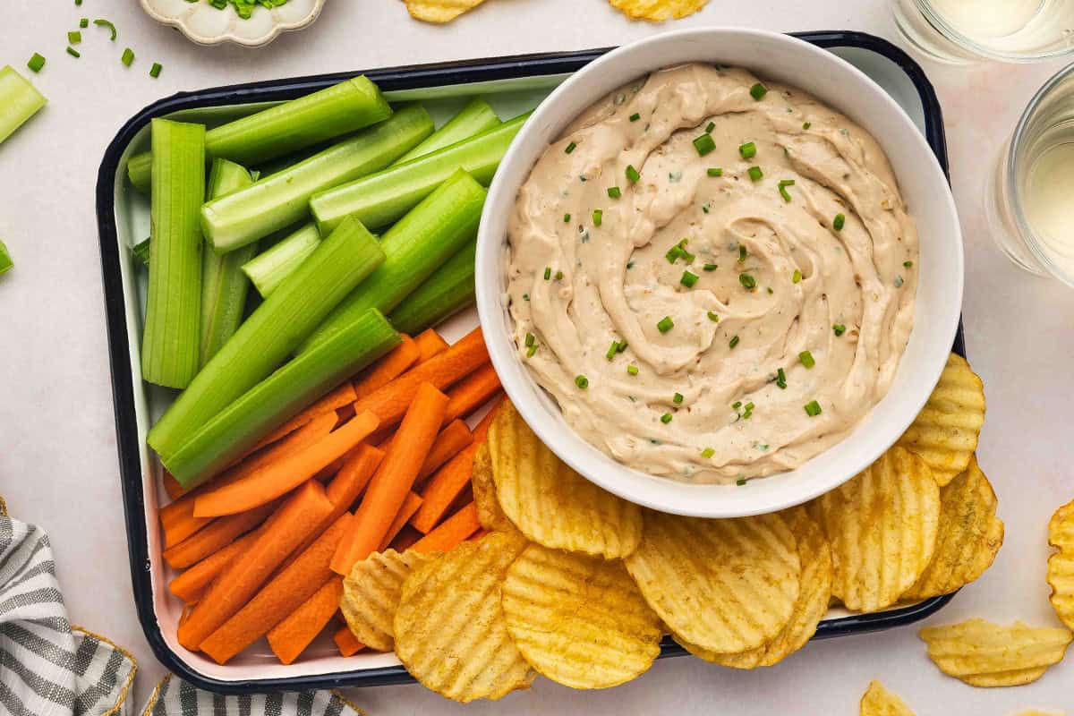 French onion dip served on a snack tray with crinkle-cut potato chips, carrot sticks, and celery