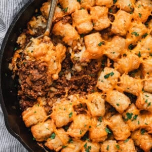 Sloppy joe tater tot skillet finished and ready to serve, with crispy golden tater tots, melted cheddar cheese, and a scoop taken out to show the saucy beef filling underneath.