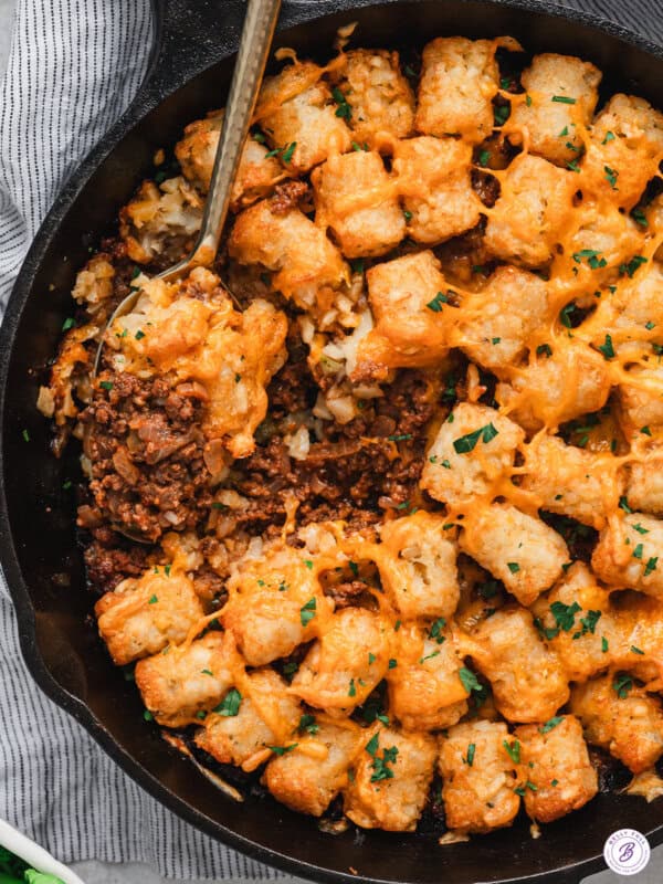 Sloppy joe tater tot skillet finished and ready to serve, with crispy golden tater tots, melted cheddar cheese, and a scoop taken out to show the saucy beef filling underneath.