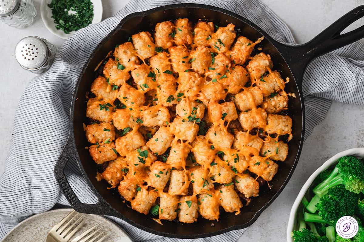 Baked sloppy joe tater tot skillet garnished with fresh parsley, showing crispy tater tots, melted cheese, and bubbling edges.