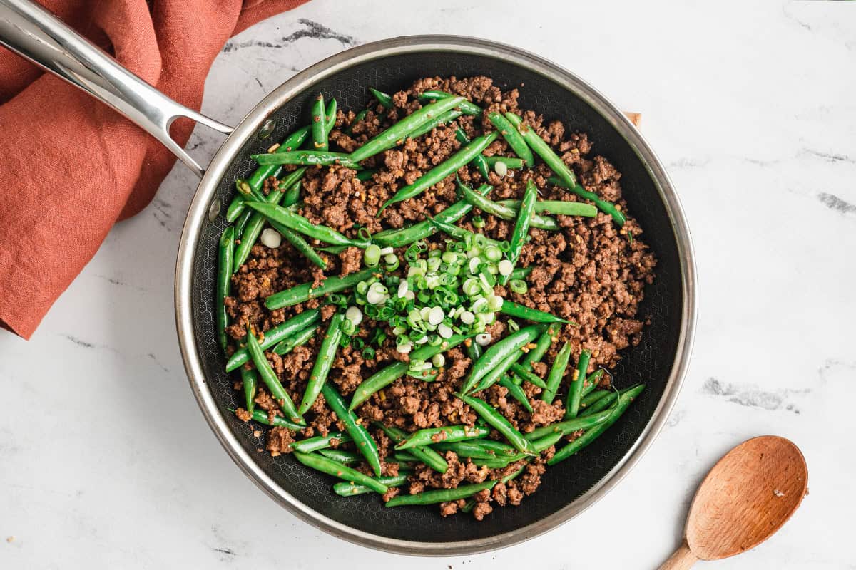 cooked ground beef crumbles, green. beans, and scallions in skillet