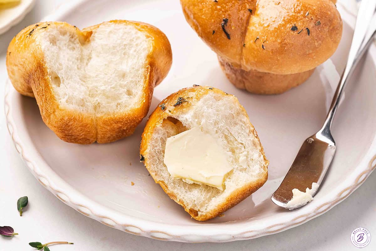 A cloverleaf roll on a plate sliced in half with butter on.