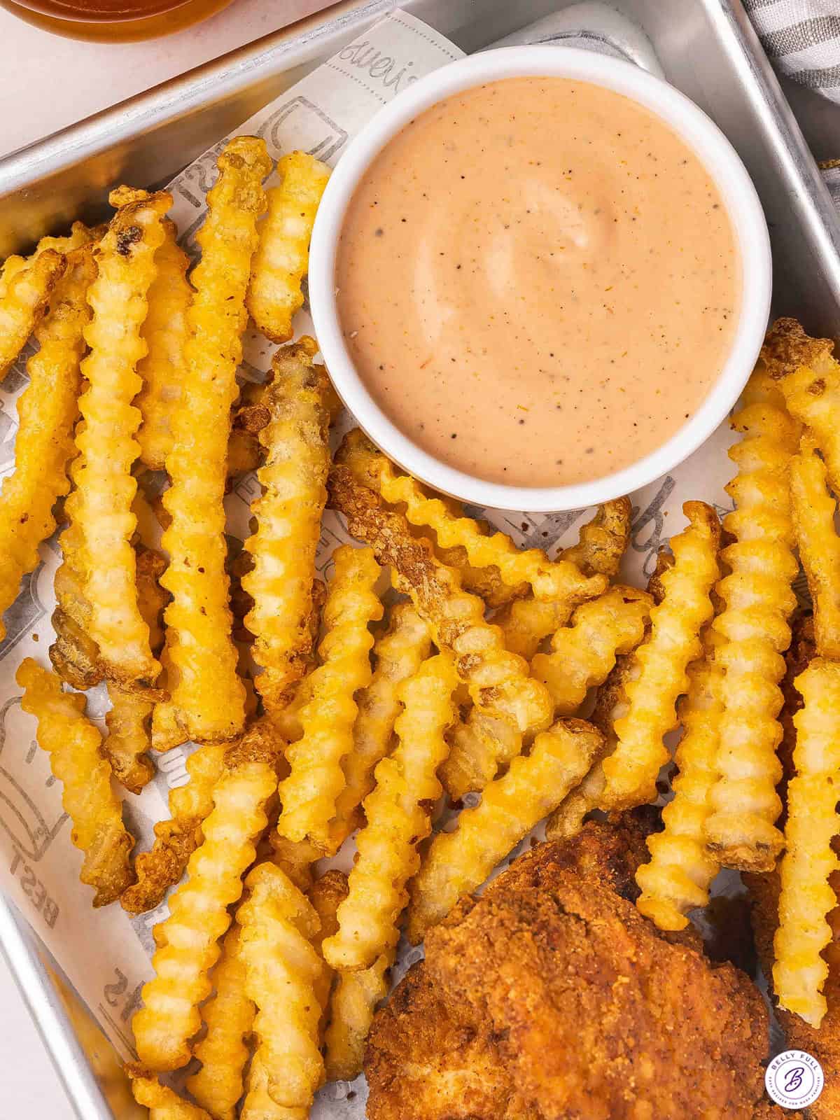 Overhead view of a pot of homemade raising cane's sauce on a tray with chicken tenders and fries.