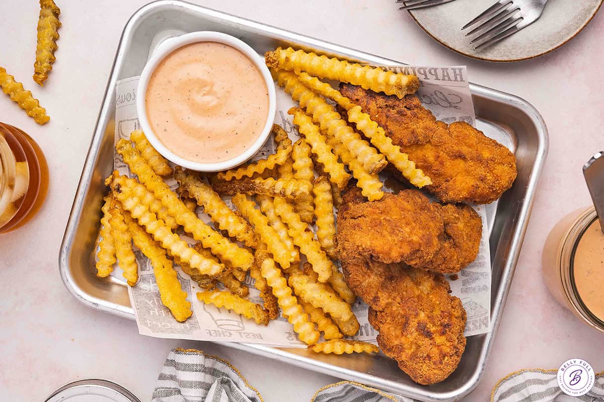 Raising cane's sauce in a bowl on a tray with fries and chicken tenders.