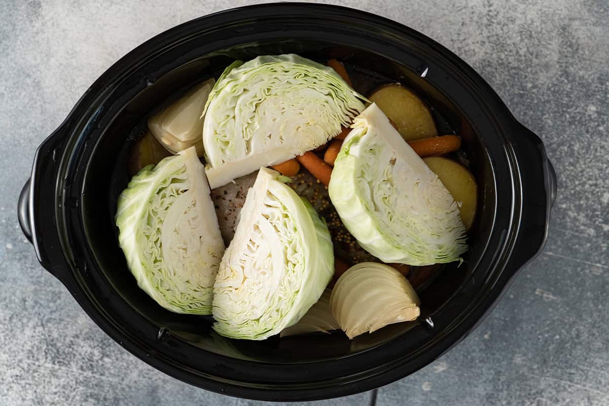 cabbage wedges on top of corned beef and vegetables inside crock pot