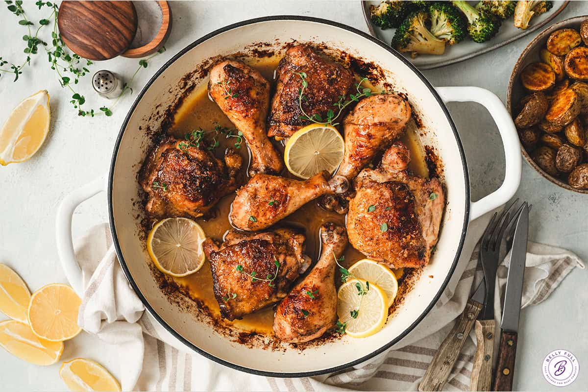 Balsamic lemon chicken in a skillet with lemon slices and thyme, surrounded by roasted potatoes and broccoli