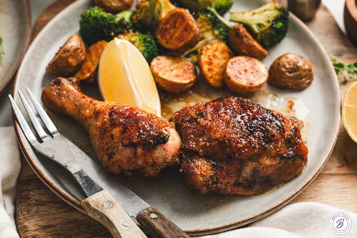 Plated balsamic lemon chicken thigh and drumstick served with roasted potatoes, broccoli, and a lemon wedge