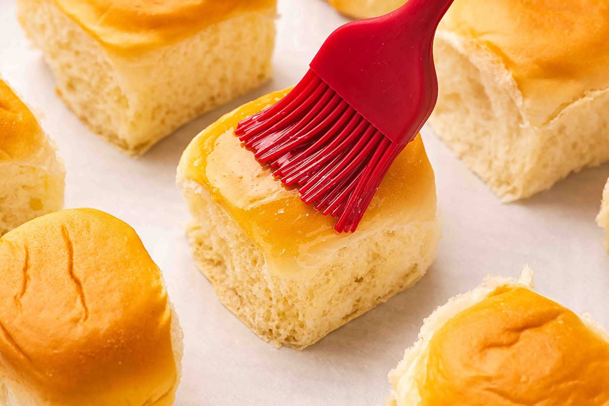 A hawaiian roll being brushed with melted butter.