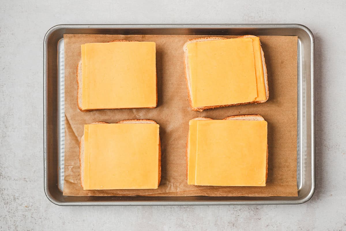 Sliced cheddar on four slices of Texas toast on a baking sheet.