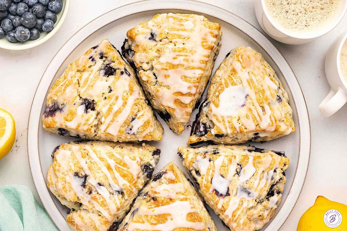 Plate of homemade lemon blueberry scones with lemon glaze served with coffee.