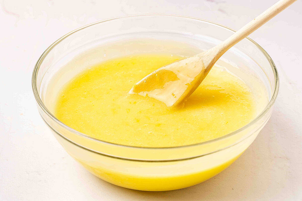Partially thickened lemon curd in a bowl after microwaving, stirred with a wooden spatula.