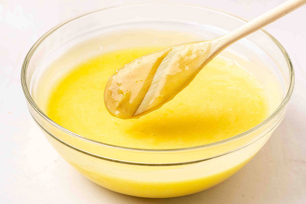 Thick, glossy lemon curd coating the back of a wooden spatula showing proper consistency.