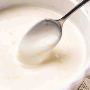 Angled overhead view of a homemade lemon glaze in a bowl with a spoon.