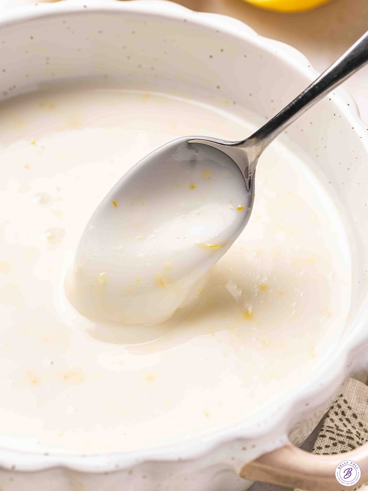 Angled overhead view of a homemade lemon glaze in a bowl with a spoon.