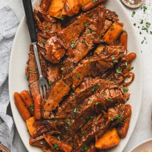 Sliced slow cooker barbecue beef brisket served with carrots, potatoes, and onions on a platter with sauce