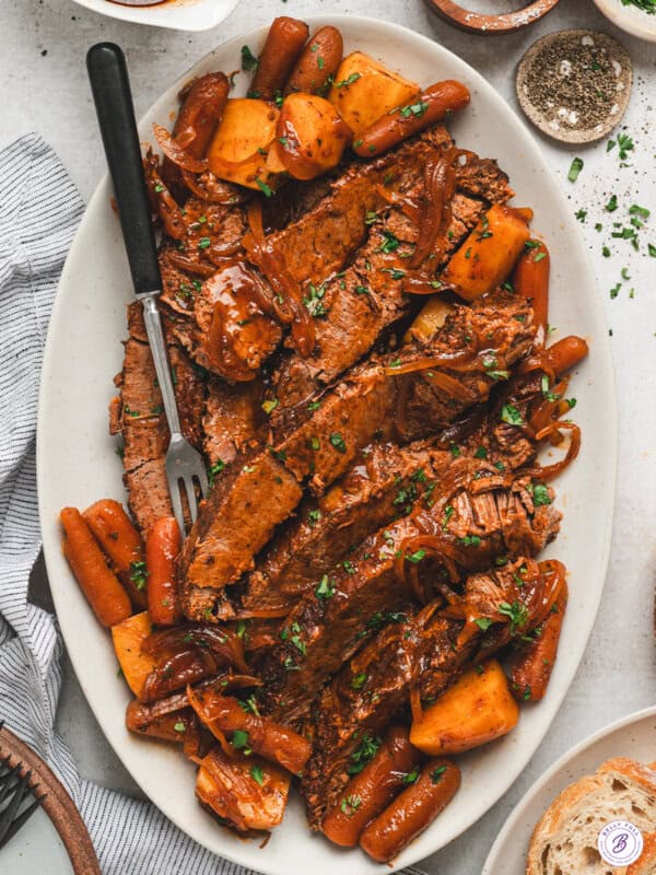 Sliced slow cooker barbecue beef brisket served with carrots, potatoes, and onions on a platter with sauce