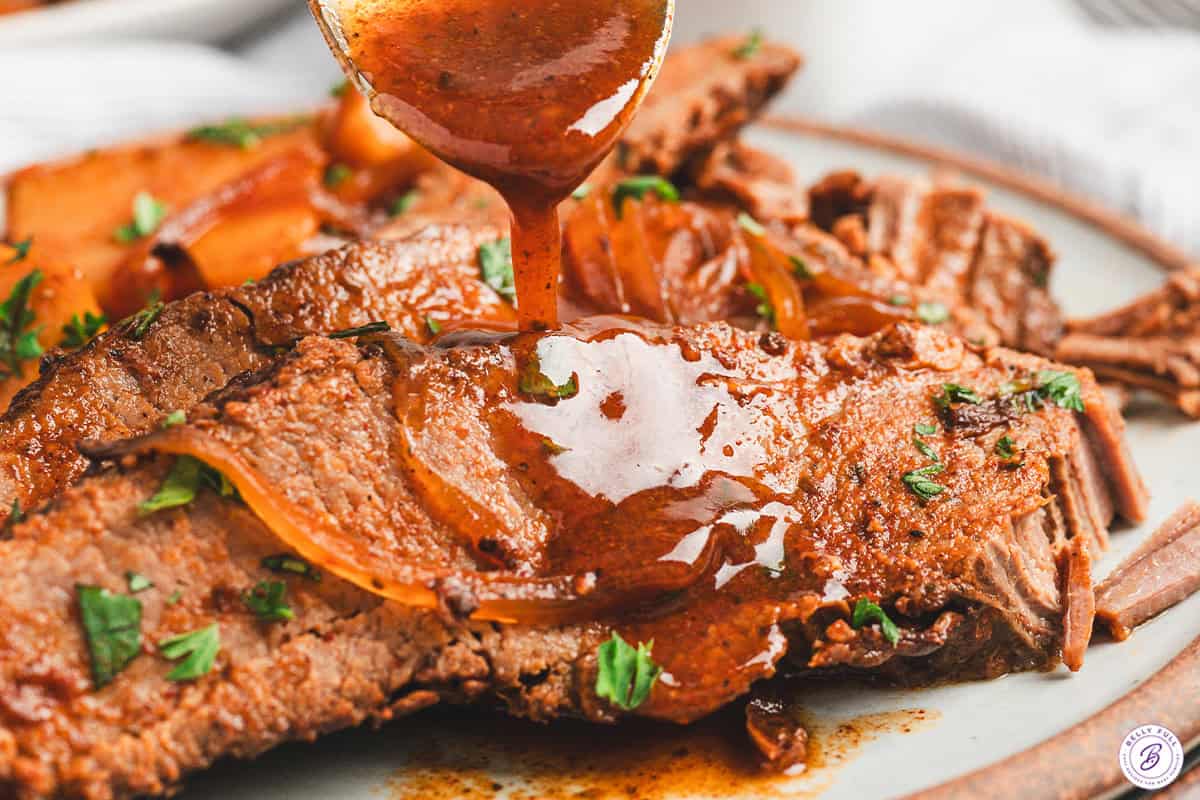 Close-up of barbecue sauce being spooned over sliced brisket for serving