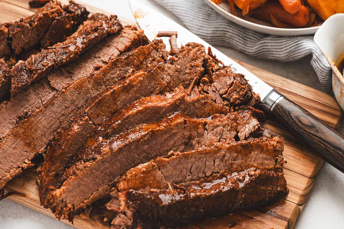 Cooked beef brisket sliced against the grain on a cutting board with juices visible