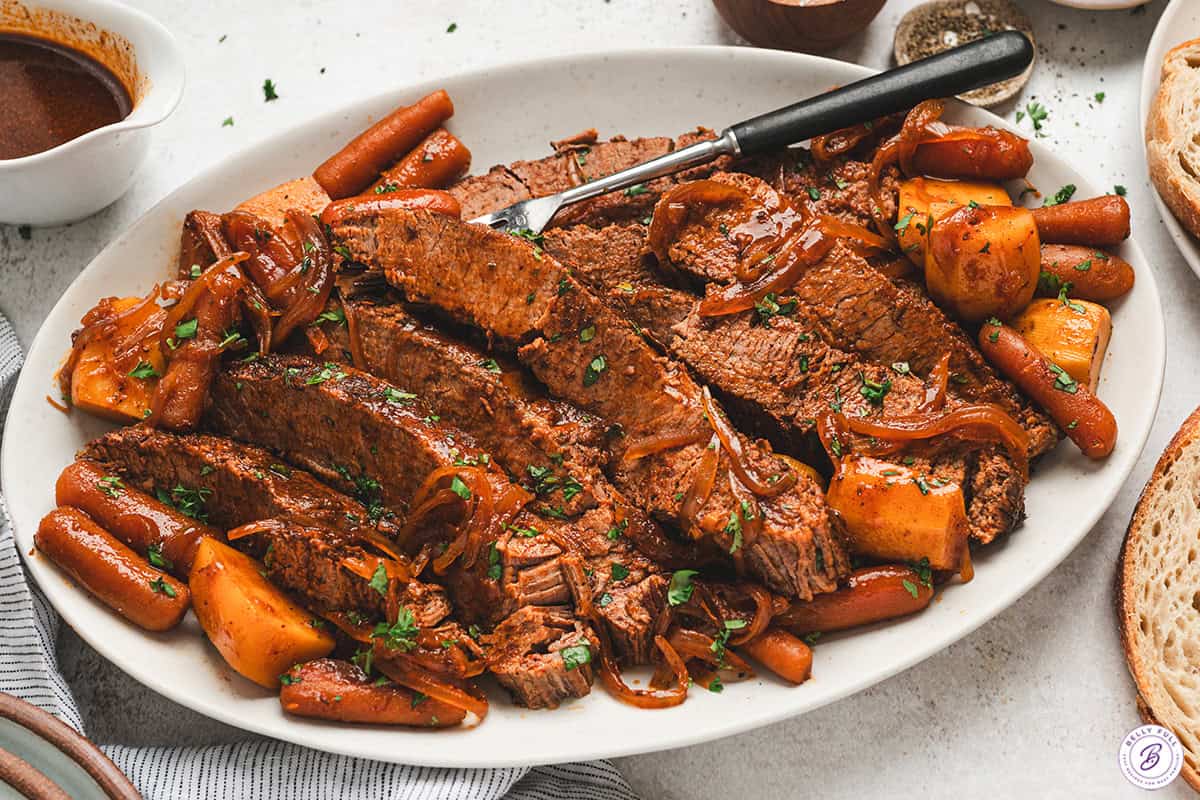 Slow cooker barbecue beef brisket served with carrots, potatoes, and onions on a platter