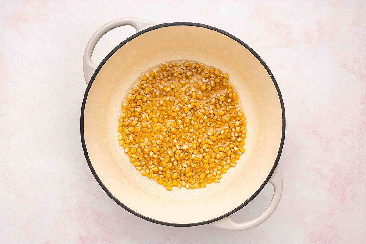 Popcorn kernels spread in a single layer in a pot before popping on the stovetop.