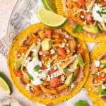 Overhead view of chicken tinga tostadas on a plate with cheese, sour cream and lime wedge toppings.