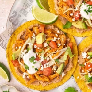 Overhead view of chicken tinga tostadas on a plate with cheese, sour cream and lime wedge toppings.