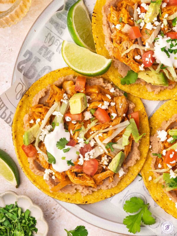 Overhead view of chicken tinga tostadas on a plate with cheese, sour cream and lime wedge toppings.