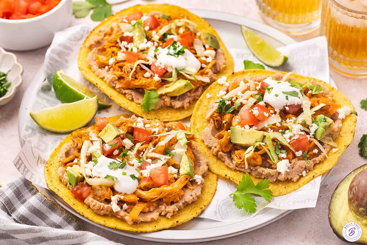 Three chicken tinga tostadas on a plate.