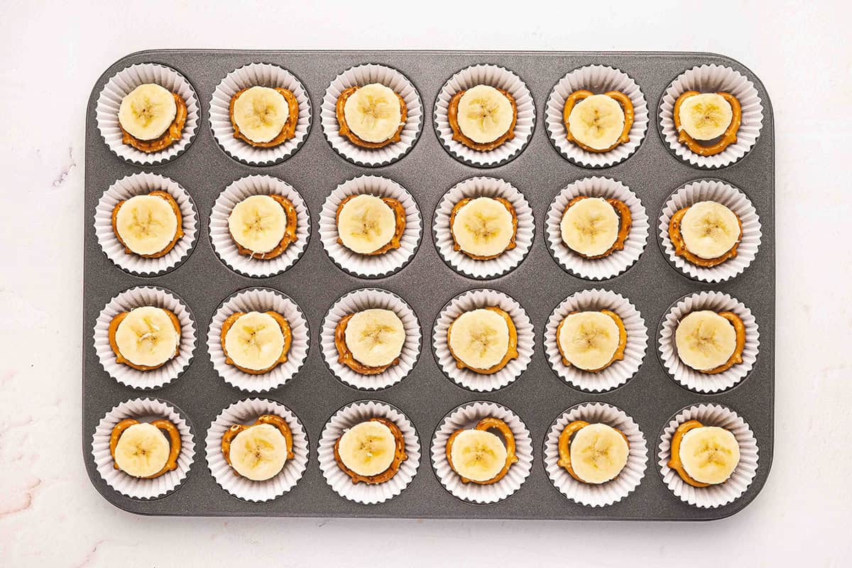 Pretzels topped with a banana slice in a mini muffin pan with muffin liners.
