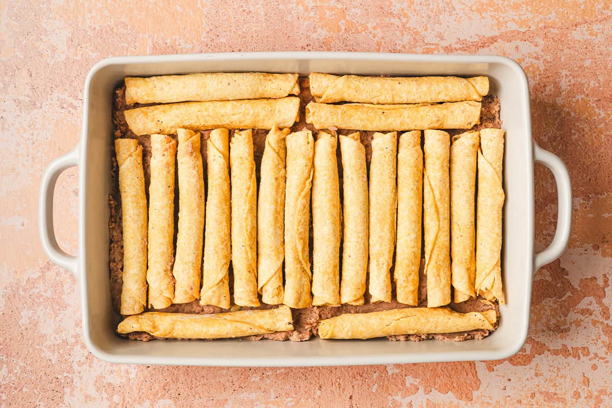 Frozen taquitos arranged in a baking dish.