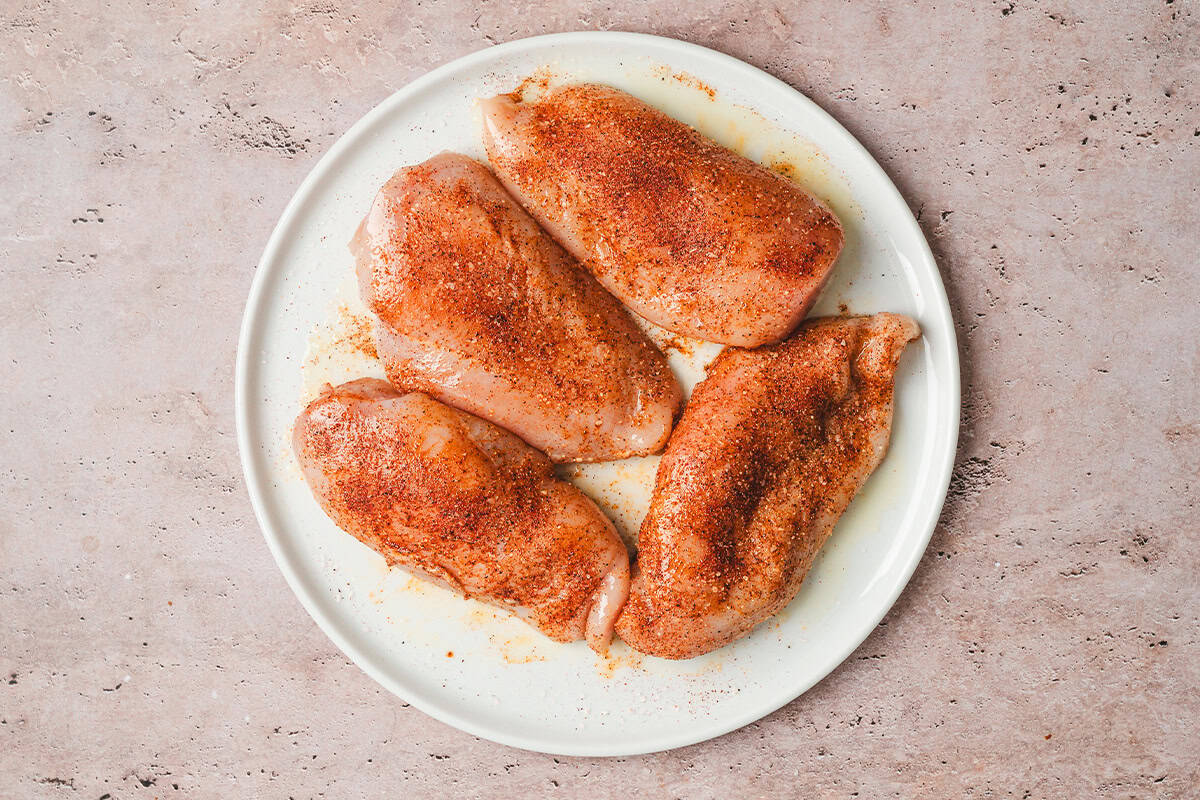 Four seasoned chicken breasts on a plate.