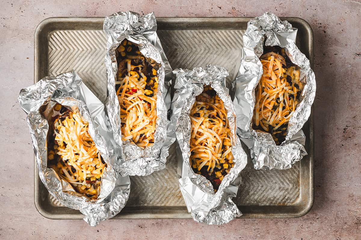 Four Southwestern Chicken Foil Packets with cheese added on a baking sheet.