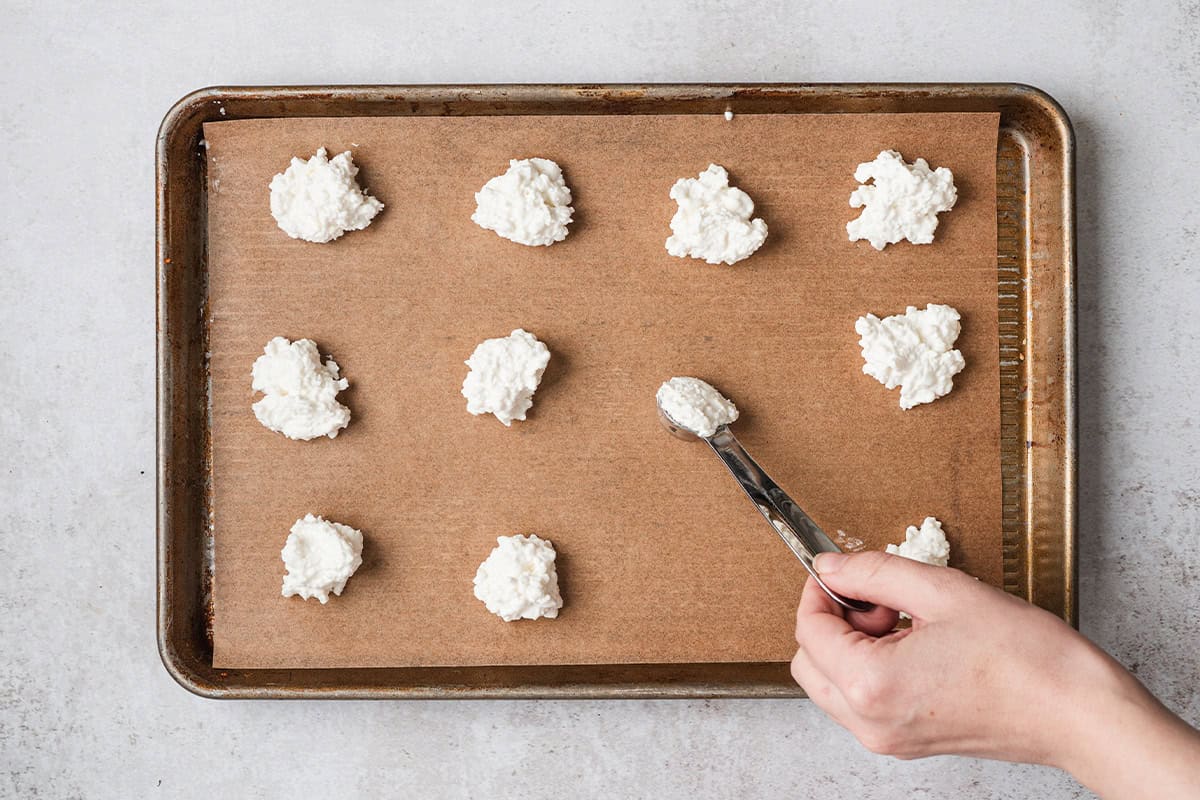 Cottage cheese being spooned onto a parchment lined baking sheet.