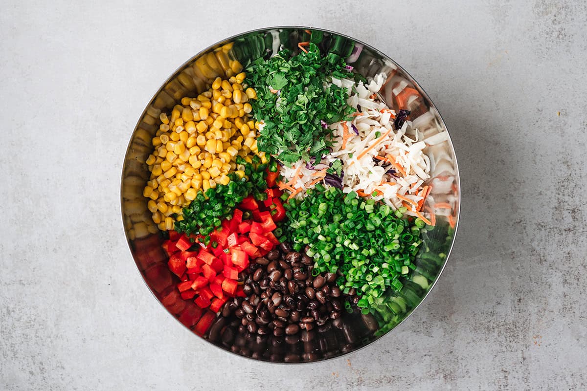 Black beans, corn, coleslaw mix, diced red bell pepper, scallions, jalalpenos, and cilantro in a bowl.