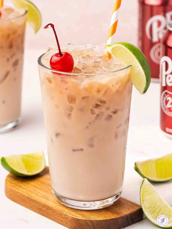 Front view of a glass of dirty soda with a lime wedge and cherry.