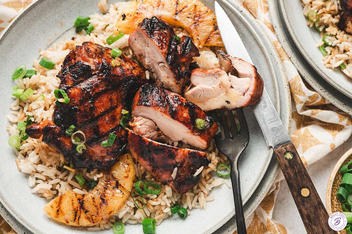 Sliced Hawaiian barbecue chicken thighs served with rice and grilled pineapple on a dinner plate