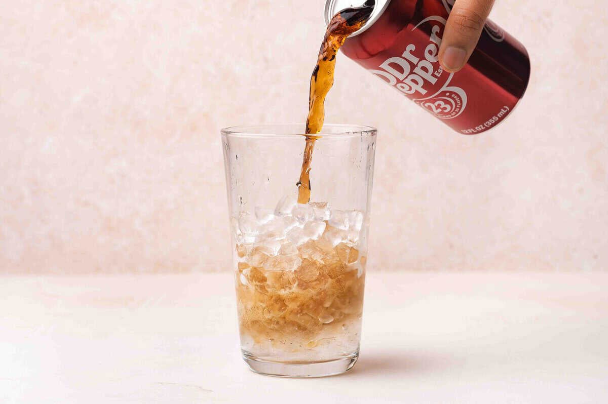 Dr pepper being poured into a glass of ice.