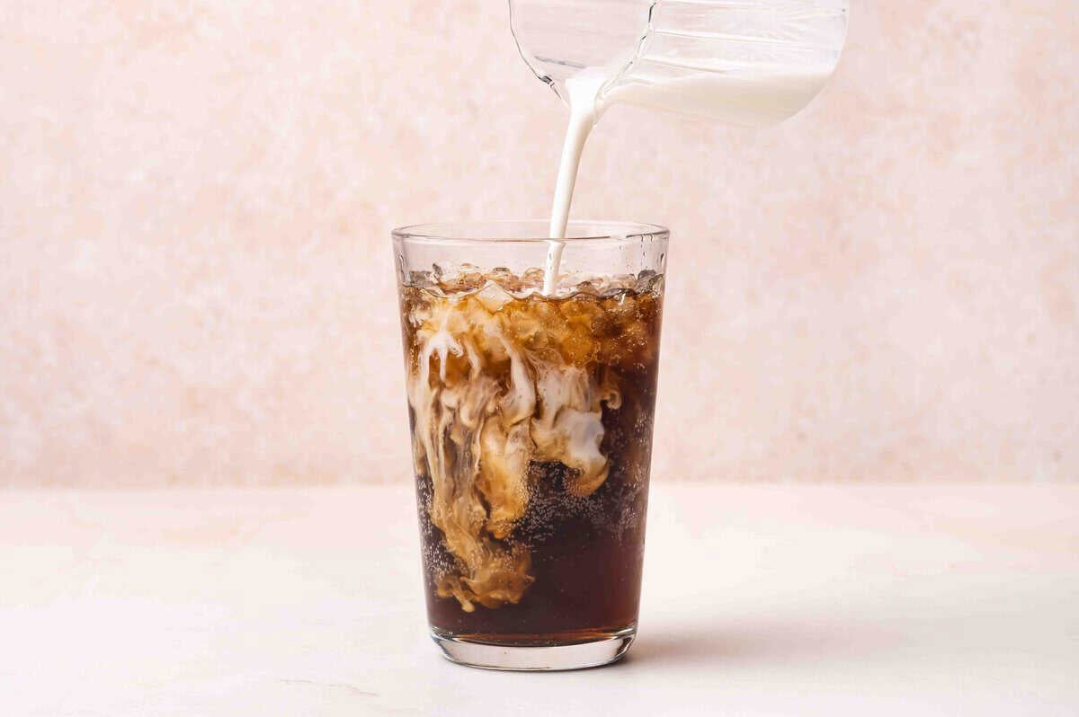 Coffee creamer being added to a glass of dr pepper.