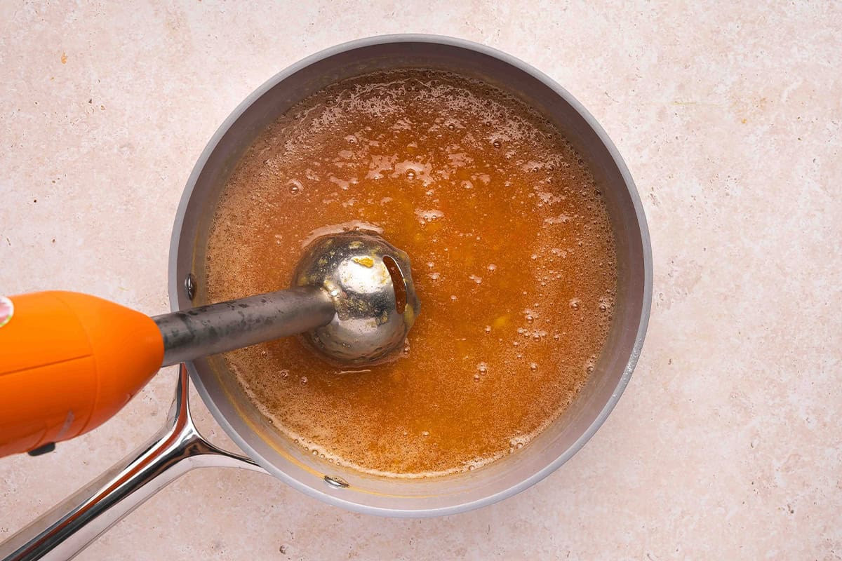 Immersion blender blending homemade peach jam in a saucepan