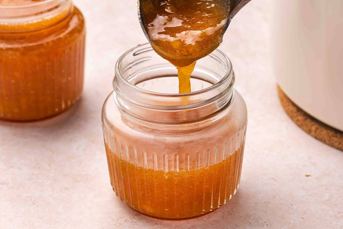 Ladle pouring peach jam into a glass storage jar
