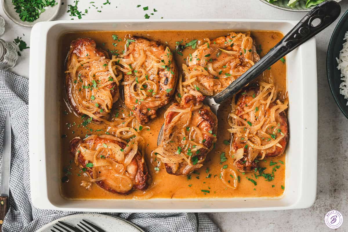 A spatula lifting a pineapple-onion pork chop out of a baking dish.