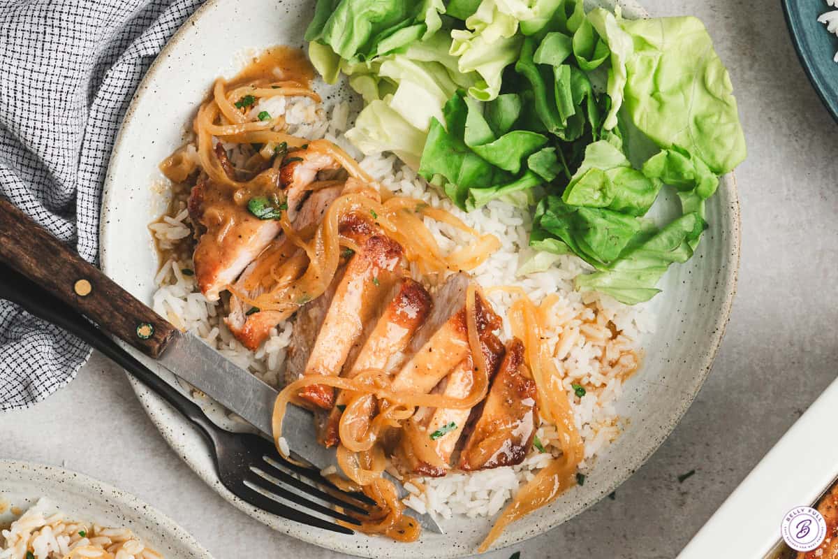 A sliced pineapple-onion pork chop on a bed of rice with a simple side salad.