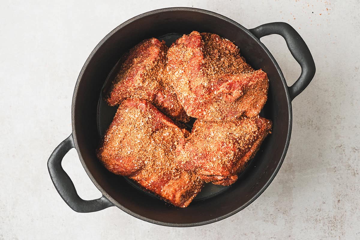 Seasoned pork shoulder pieces coated in homemade spice rub inside a Dutch oven before roasting.