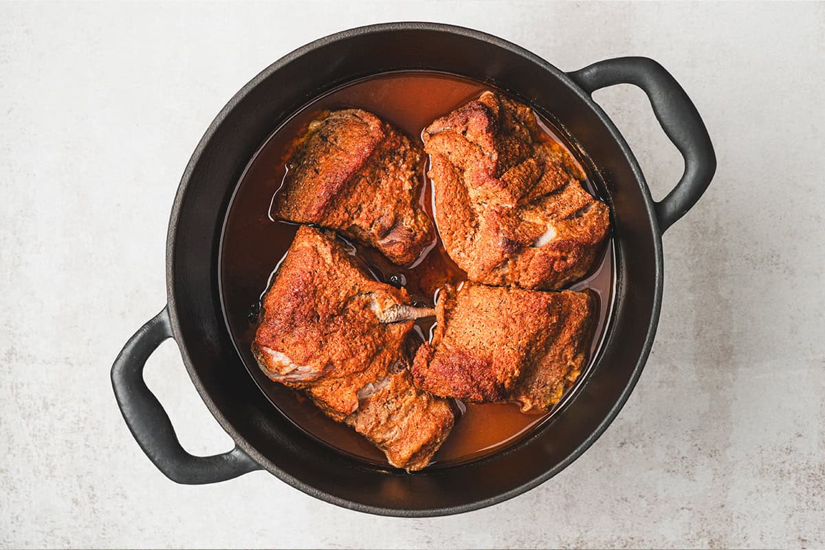 Pork shoulder roasting low and slow in cooking liquid inside a Dutch oven.