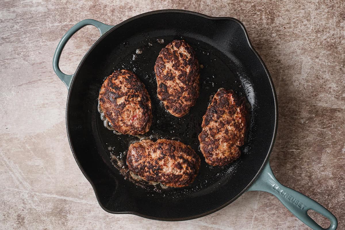Salisbury steak patties browning in a cast iron skillet until deeply golden.