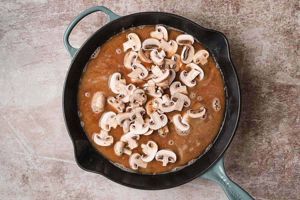 Sliced cremini mushrooms added to the brown gravy in a cast iron skillet.