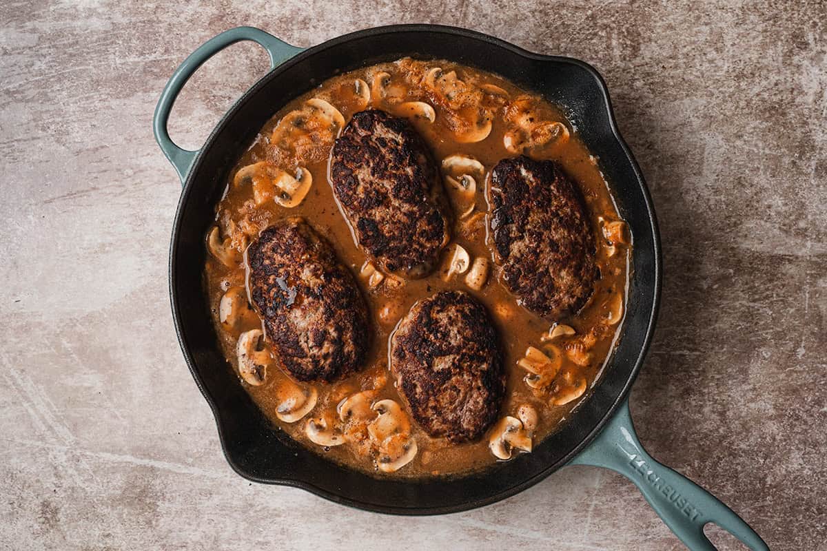 Salisbury steak patties simmering in mushroom gravy in a cast iron skillet before serving.
