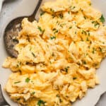 Creamy fluffy scrambled eggs topped with fresh chives and black pepper on a serving plate.