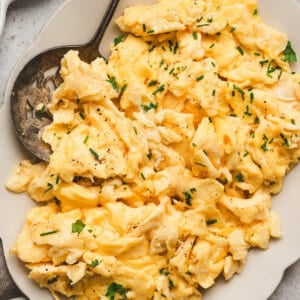 Creamy fluffy scrambled eggs topped with fresh chives and black pepper on a serving plate.