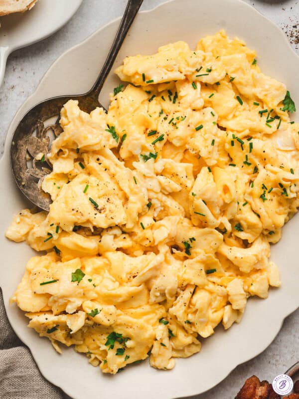 Creamy fluffy scrambled eggs topped with fresh chives and black pepper on a serving plate.